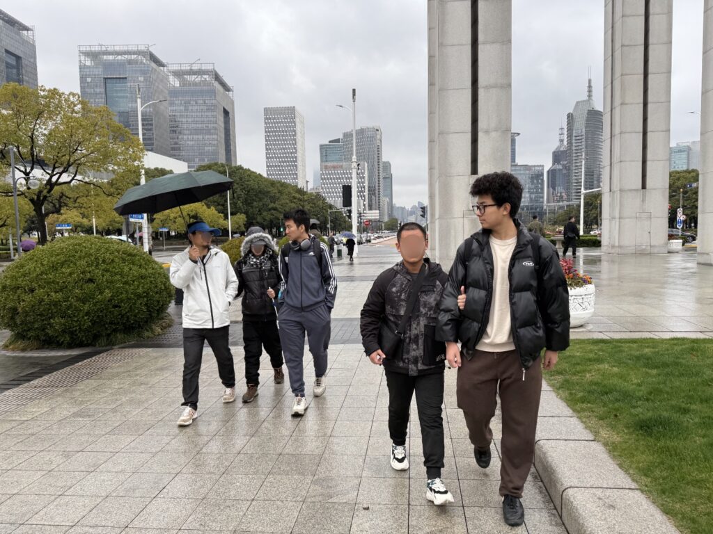 Several people walking in the rain, including the community advocate in white, the two people with visual impairments in black, and two students.