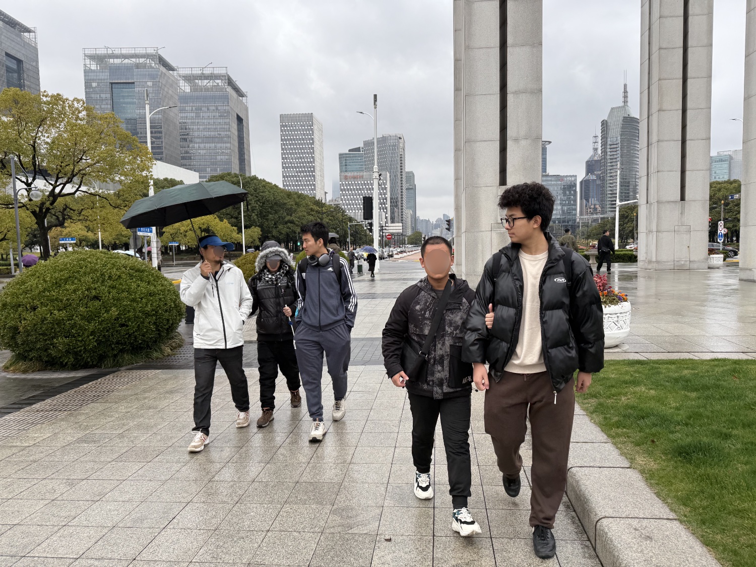 Five people walking in the rain. Two of which have visual impairments, and two students are guiding them.